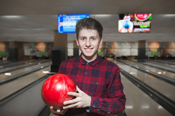 Portrait of a beautiful young man playing bowling and smiling. Positive young man with a red bowling ball in his hands. - Photo, image