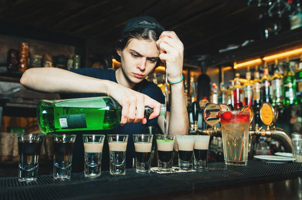Κορίτσι μπάρμαν δημιουργεί αλκοολούχα εμφάνιση στο μπαρ. Ο μπάρμαν χύνει αλκοόλ σε ποτήρια με πυροβολισμούς. - Φωτογραφία, εικόνα