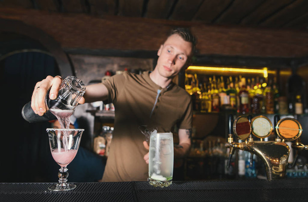 El barman crea hermosos cócteles alcohólicos en el bar de la discoteca. El barman vierte alcohol de una coctelera en un vaso
 - Foto, imagen