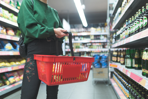 Eine Frau mit rotem Korb steht im Supermarkt. Warenkorb aus nächster Nähe. Einkaufen im Supermarkt-Konzept. - Foto, Bild