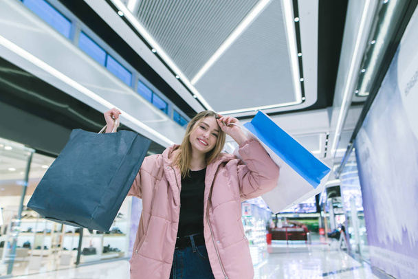 Una bionda sorridente in un bellissimo centro commerciale solleva borse della spesa. Concetto shopping
. - Foto, immagini