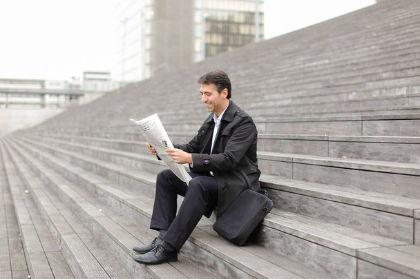 чоловічий бізнес-репетитор сидить на сходах і читає газету
 - Фото, зображення