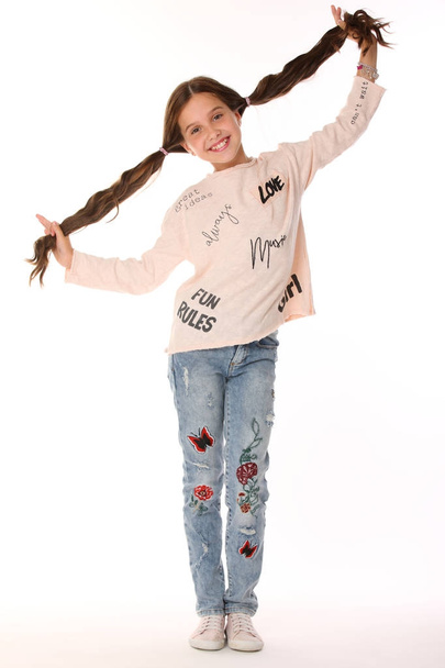 Pretty beautiful happy brunette young teen girl in blue jeans. The adorable slender smiling preteen standing in sports shoes. The image of children's summer fashion. - Photo, Image