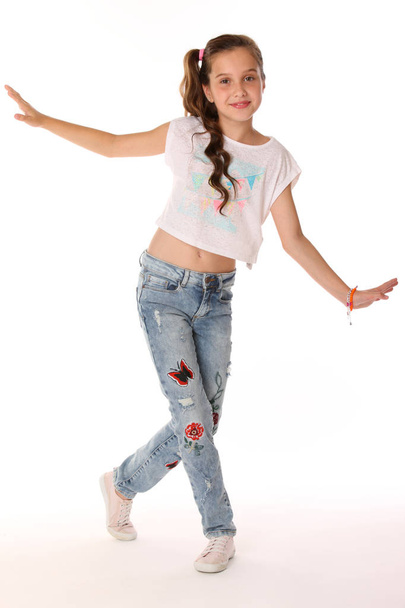 Pretty beautiful happy brunette young teen girl in blue jeans and a bare belly. The adorable slender smiling preteen standing in sports shoes. The image of children's summer fashion. - Valokuva, kuva