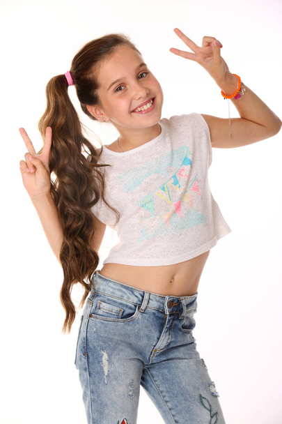Portrait of beautiful happy brunette young teen girl in blue jeans and a bare belly. The adorable slender smiling preteen is an image of children's summer fashion. - Foto, afbeelding