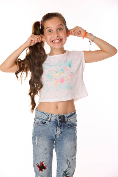 Portrait of beautiful cheerful brunette young teen girl builds a smiley face ape. The child playing tricks. Laughing preteen in blue jeans and a bare belly is an image of children's summer fashion. - Foto, imagen