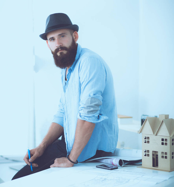 Portrait of male designer in hat with blueprints at desk - Foto, afbeelding