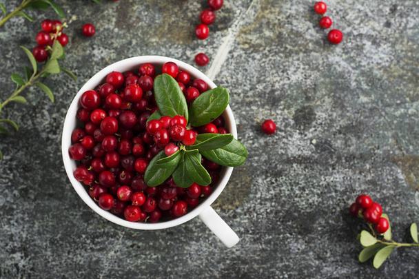 Fresh ripe forest northern cranberries or cowberry, lingonberry in ceramic cups of different size and color on a gray stone aged background for the concept of organic natural healthy food. Top View. - 写真・画像