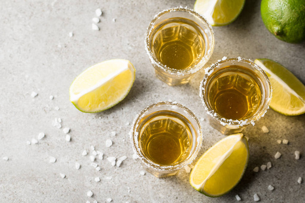 Macro focus photo of shots of golden Mexican tequila with lime and salt on wooden background. Alcoholic drink concept. - Fotó, kép