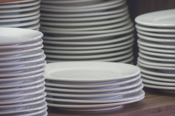 Close up stack of white clean dishes placed on wooden shelf to prepare for buffet in the morning. (Soft focus) - Photo, Image