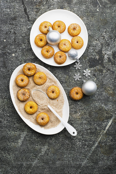 Appetizing ruddy traditional donuts with sugar and cinnamon on an oval dish on a gray grunge trendy background with a Christmas graceful neat decor with silver stars and a garland. Top View. - Foto, immagini