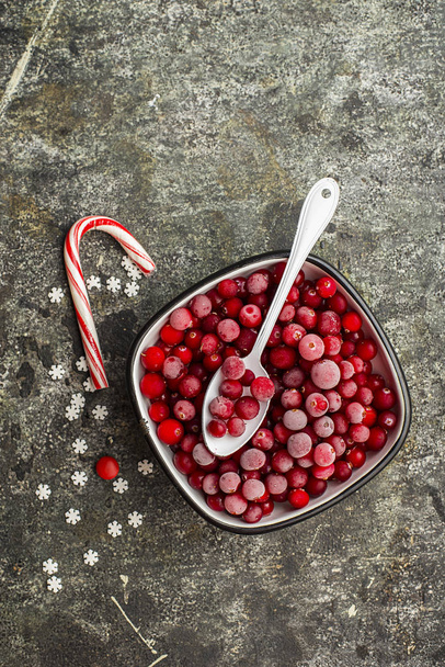 Frozen cranberries in a white enameled vintage bowl on a plain gray background with a beau enameled spoon. Top View. - Foto, immagini