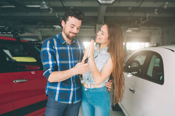 Όμορφο νεαρό ζευγάρι στέκεται στην αντιπροσωπεία επιλέγοντας το αυτοκίνητο για να αγοράσει - Φωτογραφία, εικόνα