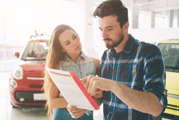 Beautiful young couple standing at the dealership choosing the car to buy - 写真・画像