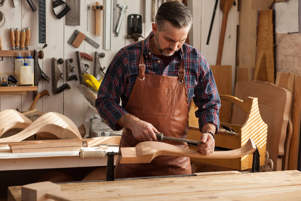 Joiner Makes Cabriole Leg for Vintage Table / Carpenter trabalha com uma plaina em uma oficina para a produção de móveis vintage. Ele faz a perna de cabriole para uma mesa no estilo de Luís XV e Rainha Ana
 - Foto, Imagem
