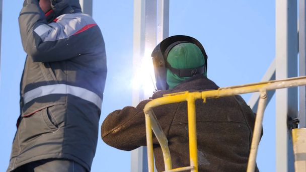 Stavební dělníci pracují na lešení, člověk pracující na práce ve výškách s modrou oblohou na staveništi. Pracovník pomocí elektrické kolo broušení na ocelové konstrukci v továrně. Práce na vysoké úrovni - Fotografie, Obrázek