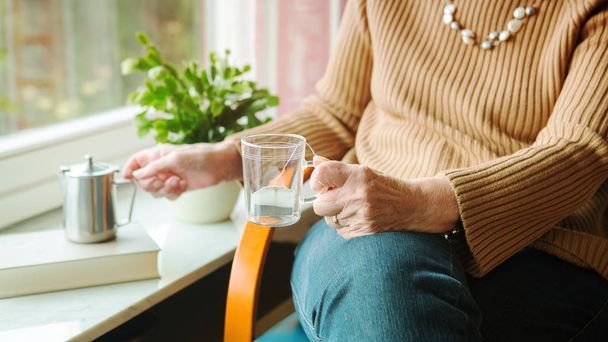 vanhempi nainen kaatamalla teetä lasiin ja istuu Windo
 - Valokuva, kuva