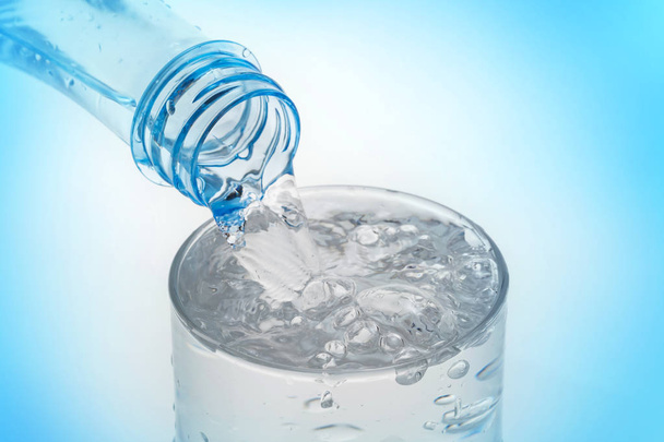 Verter agua de la botella en vidrio sobre fondo azul
. - Foto, imagen