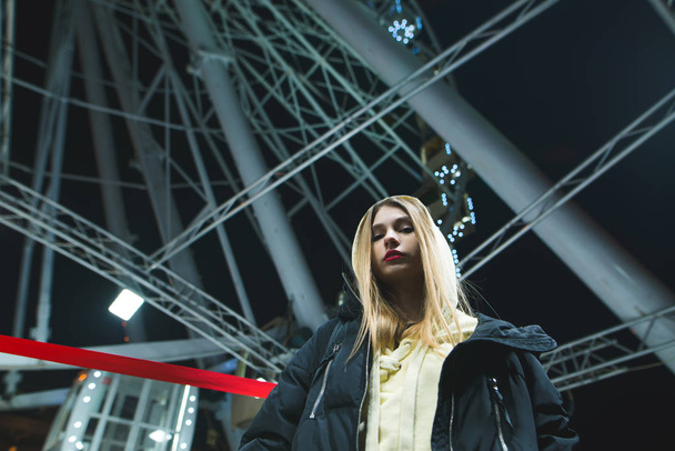Portrait of a blonde girl with metal construction of the Ferris wheel on background - Фото, зображення
