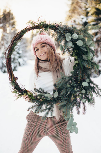 Blonde young lady with christmas wreath in winter forest - Fotoğraf, Görsel