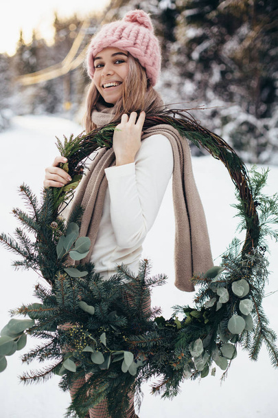 Blonde young lady with christmas wreath in winter forest - Foto, afbeelding