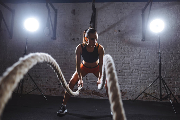 Young woman working out with battle ropes in cross fit gym - Fotoğraf, Görsel