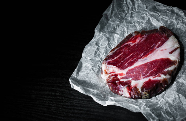 piece of raw meat beef steak on paper on dark wooden background with copy space. - Foto, Imagem
