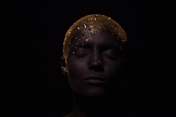 Portrait of a beautiful woman with creative body art glowing make up. Face is colored with black paint. - Fotó, kép