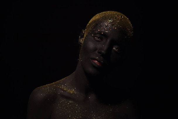 Portrait of a beautiful woman with creative body art glowing make up. Face is colored with black paint. - Foto, Imagem