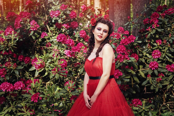 mooie jonge vrouw met mooie kapsel en lichte make-up staande in rhododendron bloemen tuin. buiten zomer schoot. kopie ruimte. - Foto, afbeelding