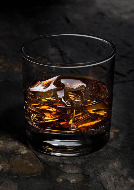 Elegant glass of whiskey with ice cubes on stone - Фото, изображение