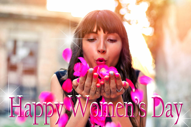 schöne brünette Frau mit Blumen, die Blütenblätter aus ihren Händen wehen. fröhlicher Text zum Internationalen Frauentag mit verschwommenem Hintergrund  - Foto, Bild
