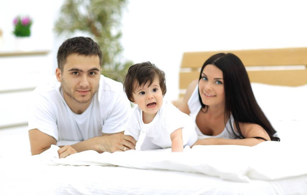 Portret van gelukkige jonge familie samen in bed liggen - Foto, afbeelding