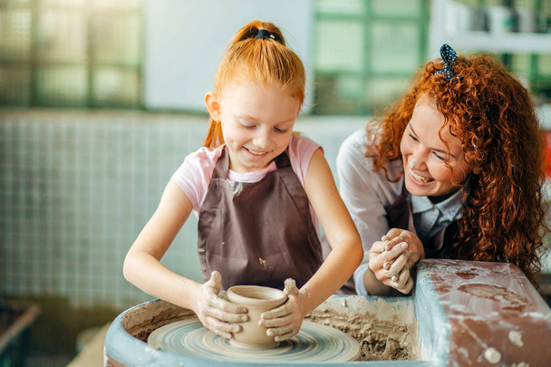 redhead mother and her child daughter moulding with clay on pottery wheel - Fotografie, Obrázek