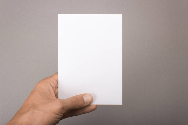 Blank postcard in hand on a gray background. Leaflet A6 mockup - 写真・画像