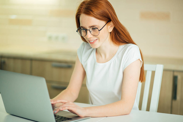 Kaunis nuori nainen hymyilee ja katselee kannettavan tietokoneen näyttöä
 - Valokuva, kuva