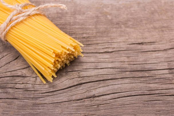 Stack of raw yellow long spaghetti on an old wooden background.  - Фото, изображение
