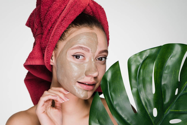 cute young girl with a red towel on her head enjoying a spa, face clay mask against acne - Foto, Imagem