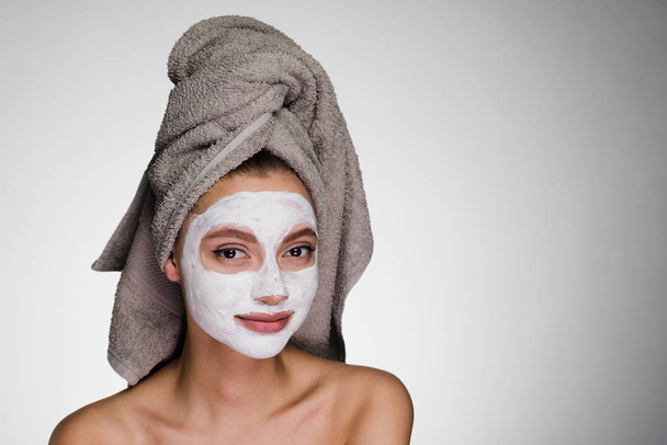 lovely young girl with a towel on her head applied a white nutritious mask to her face - Foto, imagen