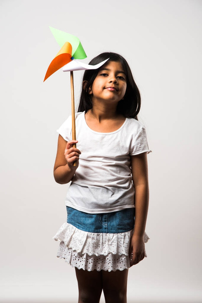 indian girl with paper windmill toy made up of tricolour or indian flag colours. Saluting, looking at camera or with red heart toy, celebrating 26 January republic day or 15 august independence day - Zdjęcie, obraz
