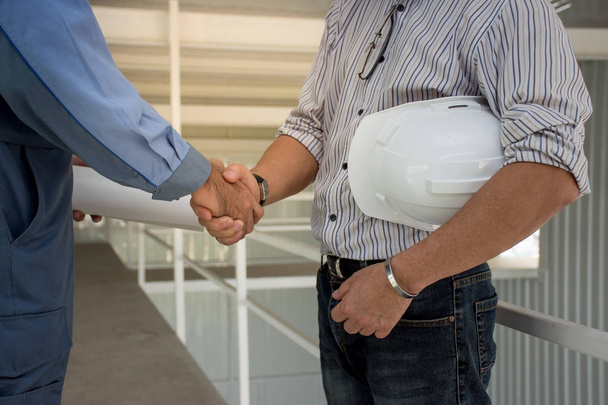 Две профессиональные инженерные команды в белом шлеме пожимают друг другу руки на стройке
. - Фото, изображение