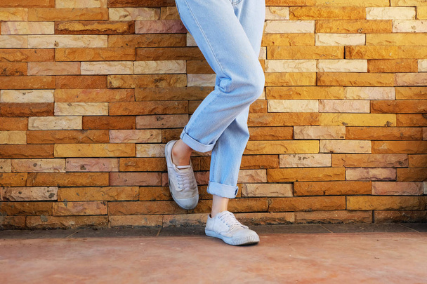 Old White Shoes. Woman Wear White Sneaker and Blue Jeans on Orange Brick Wall Background Great for Any Use. - Fotografie, Obrázek