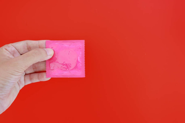 Hand holding male condom on red background with copy space for contraception and safety sex concept - Fotó, kép
