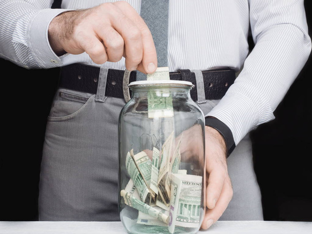 transparent glass jar that is used by a young man as a piggy bank - Photo, Image