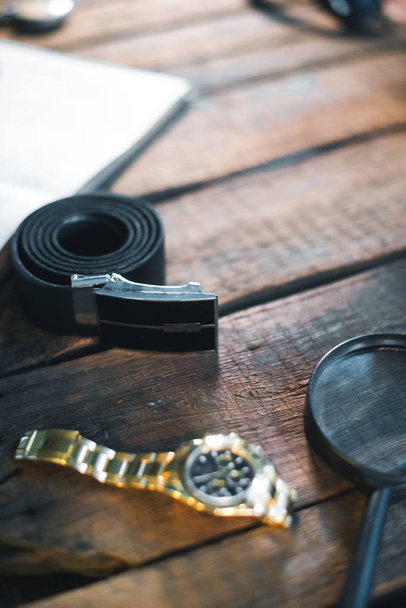 belt, watch and magnifying glass on wooden table - Zdjęcie, obraz