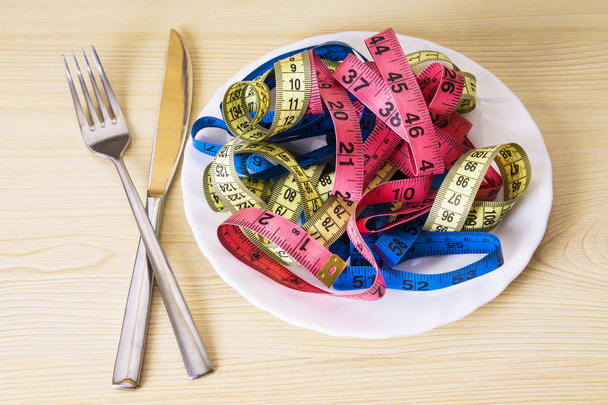 plate with tape measures and fork and knife, concept of diet and slimming - Foto, Bild