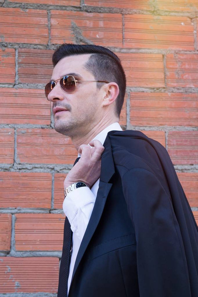 Man in suit and brick background with jacket on shoulder - Fotografie, Obrázek