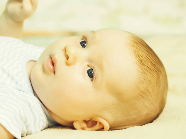 Cute baby boy infant innocent child with blue eyes and blond hair lies awake on back - Foto, Imagen