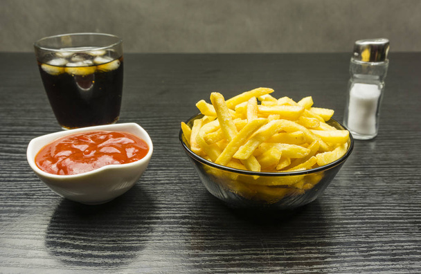Bol avec frites salées et ketchup et un verre de cola avec de la glace sur la table
. - Photo, image