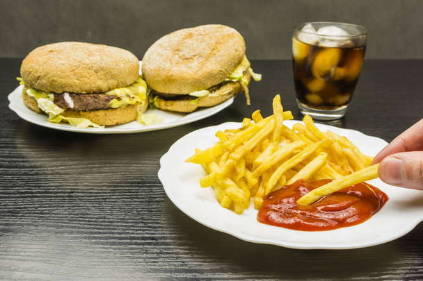French fries and ketchup on a plate and a burger and cola with ice in a glass. - Photo, Image